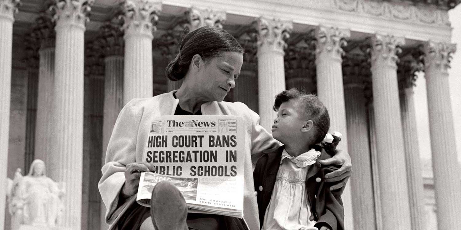 Black woman holds newspaper of Brown v Board USC decision